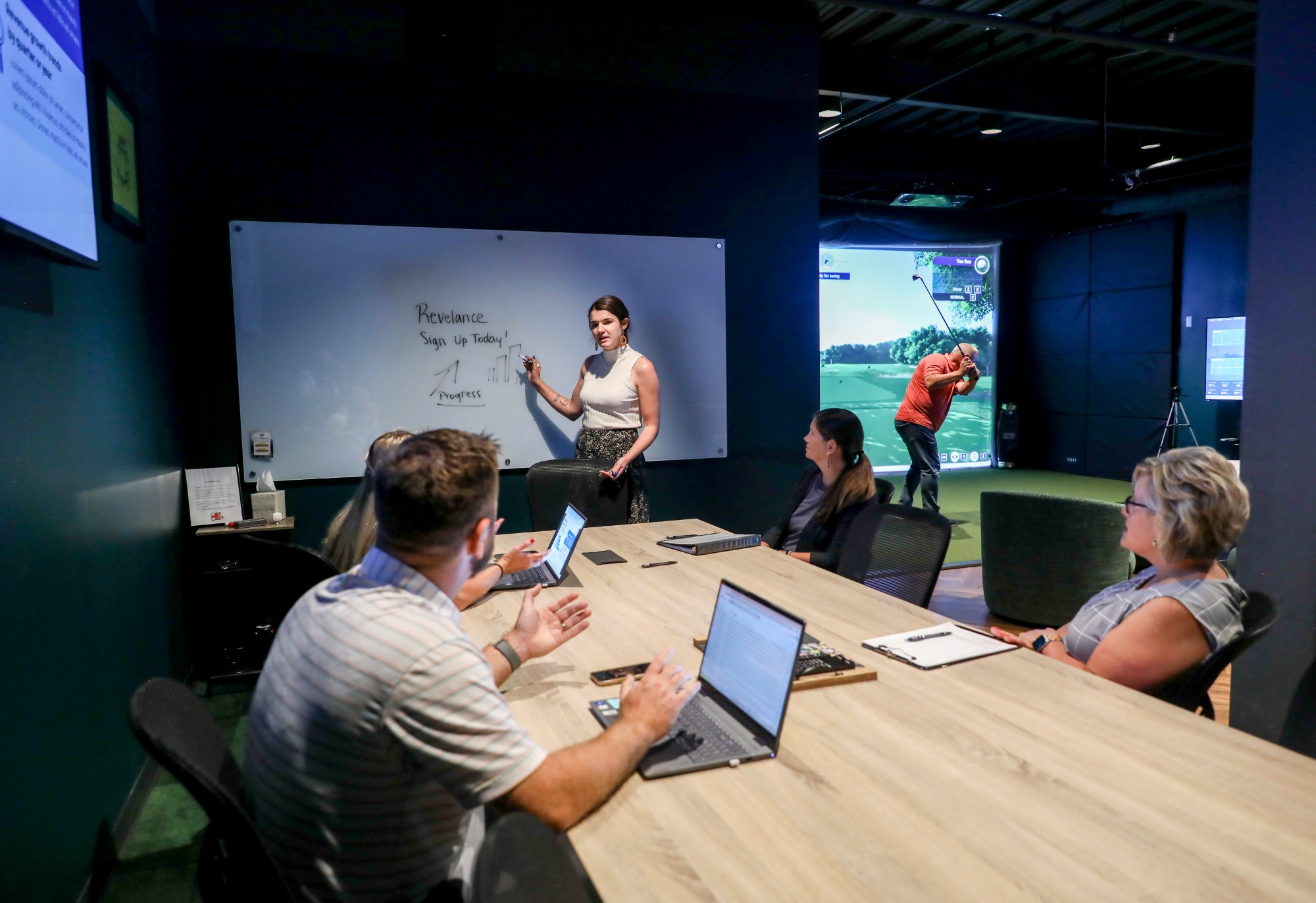 Corporate presentation on whiteboard in Emergency 9 conference room with golf simulator running in background